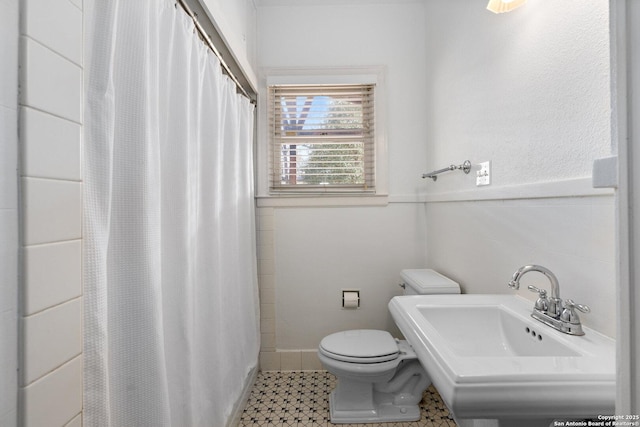 full bath with toilet, a wainscoted wall, tile patterned floors, curtained shower, and a sink