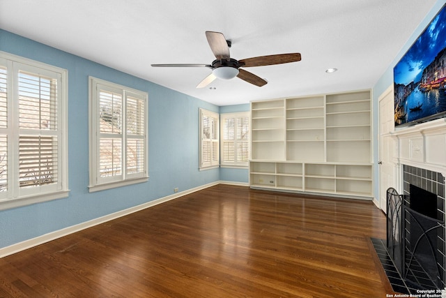 unfurnished living room with a tile fireplace, ceiling fan, baseboards, and wood finished floors