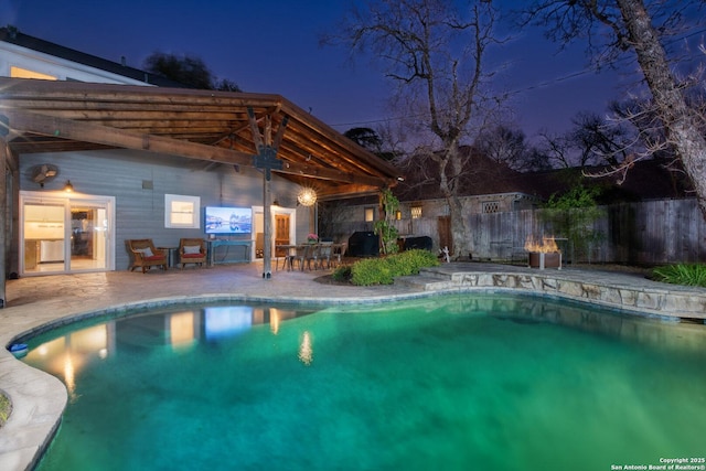 pool at night featuring a patio, fence, and a fenced in pool