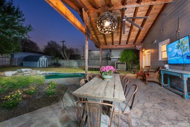 view of patio featuring a storage shed, a fenced backyard, ceiling fan, an outbuilding, and outdoor dining area