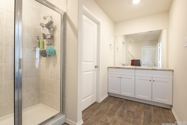 full bathroom with double vanity, a stall shower, baseboards, and wood finished floors