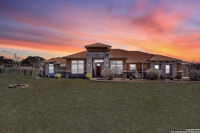 prairie-style house featuring stone siding, fence, and a front lawn