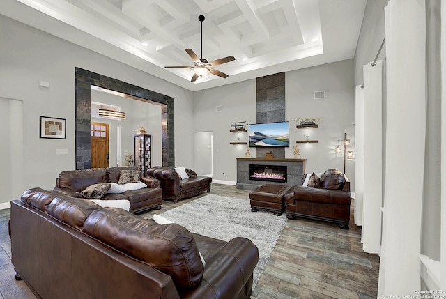 living room with a towering ceiling, ceiling fan, a tile fireplace, coffered ceiling, and baseboards