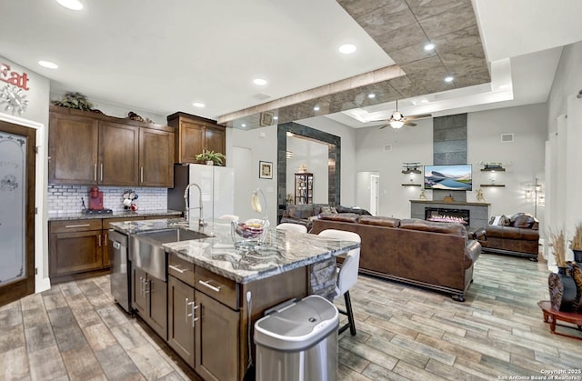 kitchen with a tile fireplace, a sink, freestanding refrigerator, light stone countertops, and a raised ceiling