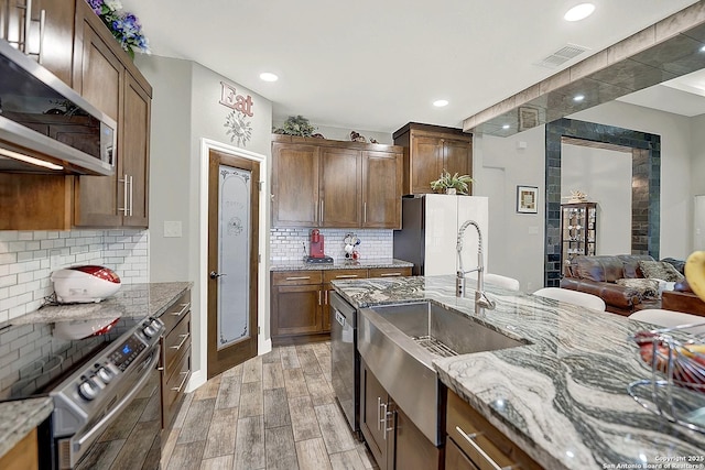 kitchen featuring light stone counters, stainless steel appliances, a sink, visible vents, and wood tiled floor