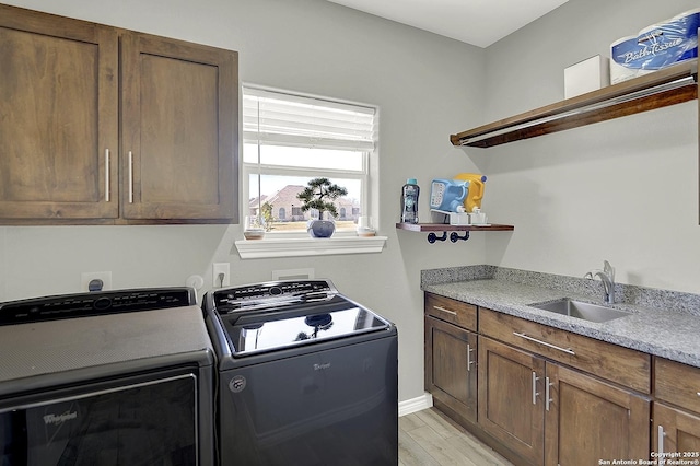 clothes washing area featuring cabinet space, light wood finished floors, a sink, and independent washer and dryer