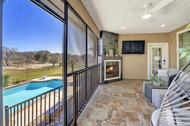 sunroom with a ceiling fan and a lit fireplace