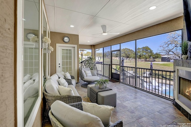 sunroom featuring a warm lit fireplace and ceiling fan