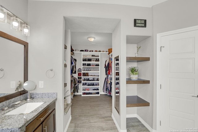 bathroom featuring a spacious closet, vanity, baseboards, and wood finished floors