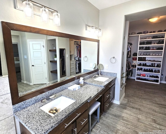 bathroom featuring double vanity, a walk in closet, a sink, and wood finished floors