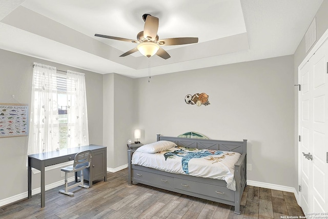 bedroom with wood finished floors, a raised ceiling, a ceiling fan, and baseboards