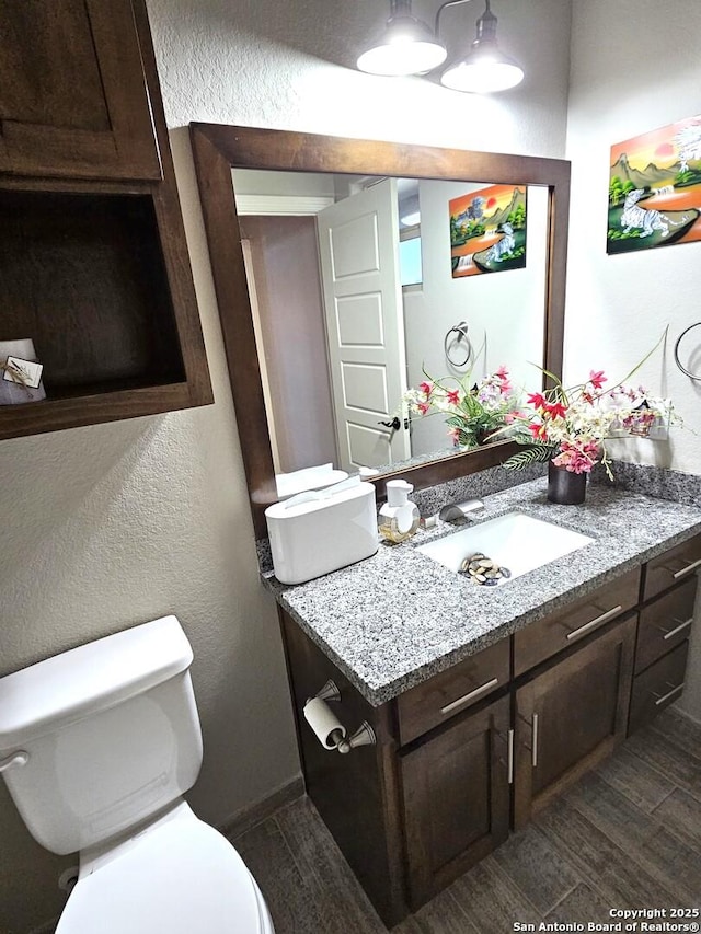 half bath with a textured wall, wood finished floors, vanity, and toilet