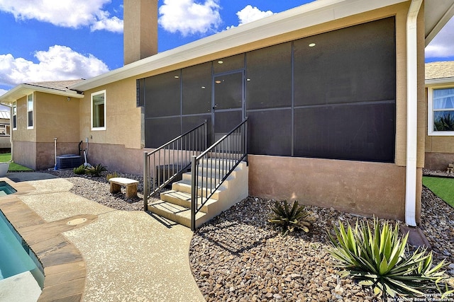 rear view of property featuring a chimney, stucco siding, a pool, a sunroom, and cooling unit