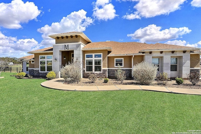 prairie-style home with stone siding, a front yard, fence, and stucco siding