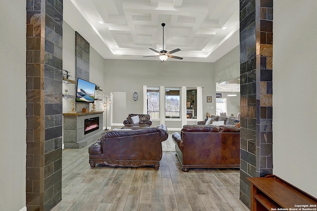 living room featuring ceiling fan, a high ceiling, coffered ceiling, wood finished floors, and a fireplace