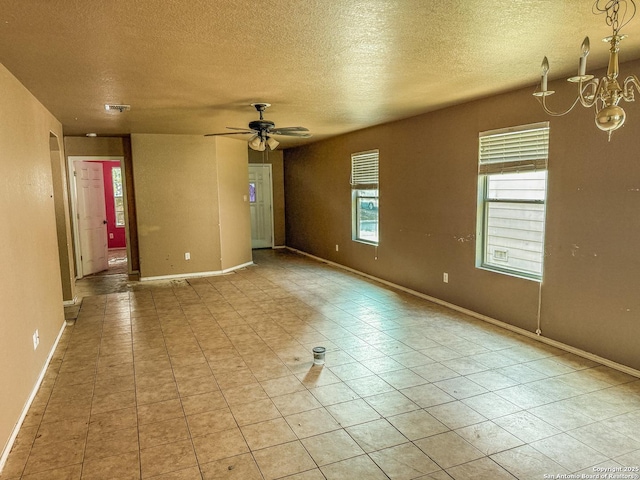 empty room featuring light tile patterned floors, baseboards, a textured ceiling, and ceiling fan with notable chandelier