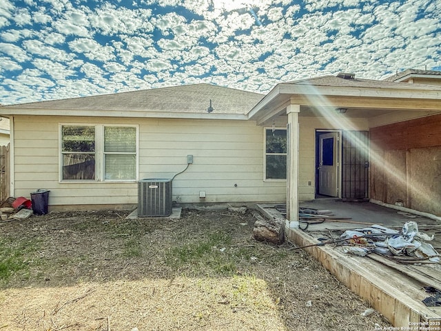 back of house featuring central AC unit and roof with shingles