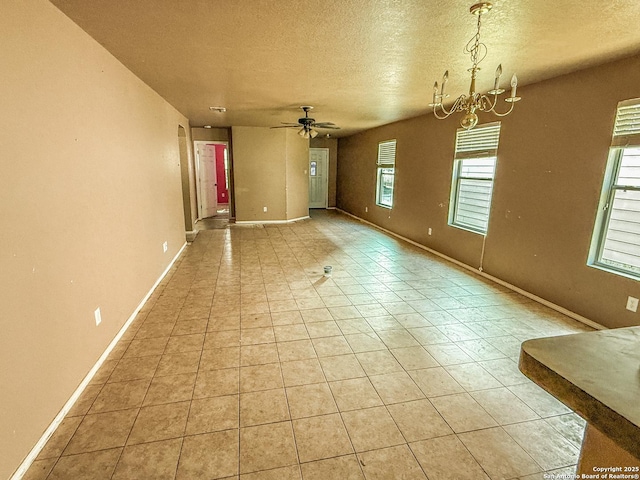 empty room with light tile patterned flooring, baseboards, a textured ceiling, and ceiling fan with notable chandelier