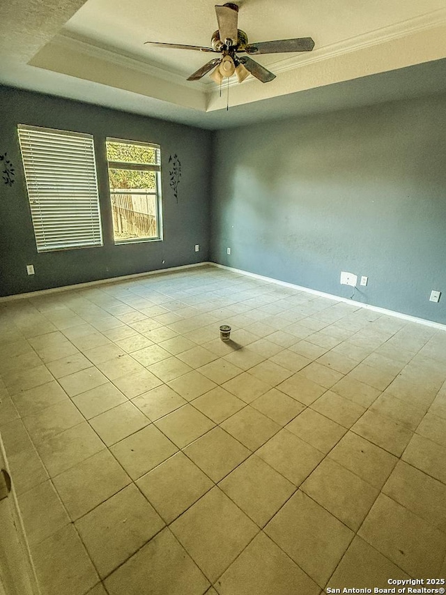 empty room featuring crown molding, a raised ceiling, a ceiling fan, and baseboards