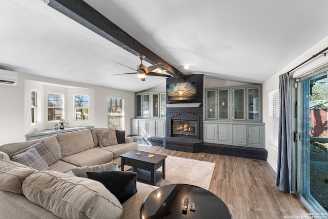 living area with vaulted ceiling with beams, light wood finished floors, a wall mounted AC, a brick fireplace, and a healthy amount of sunlight