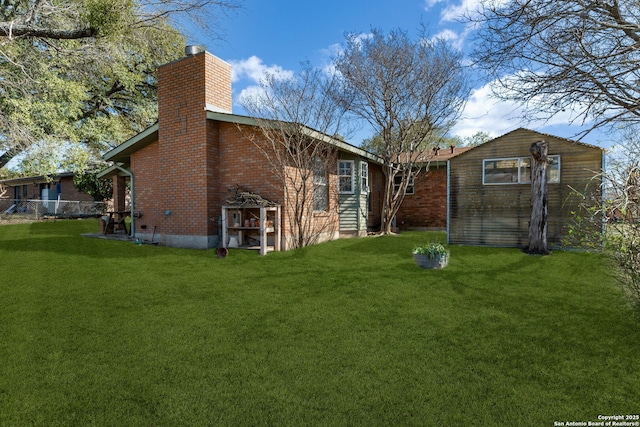 back of house with a chimney, fence, a lawn, and brick siding