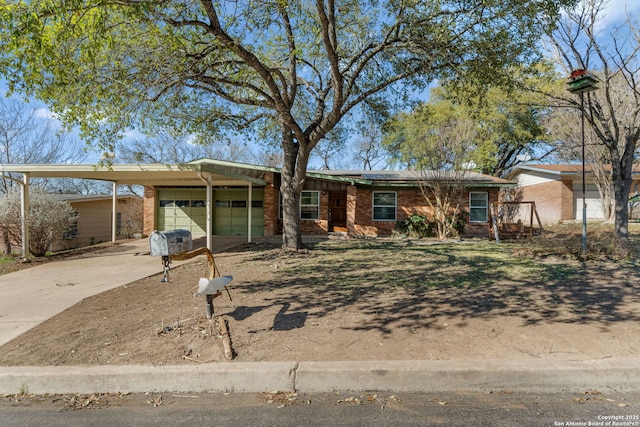 ranch-style home with brick siding, solar panels, concrete driveway, an attached garage, and a carport