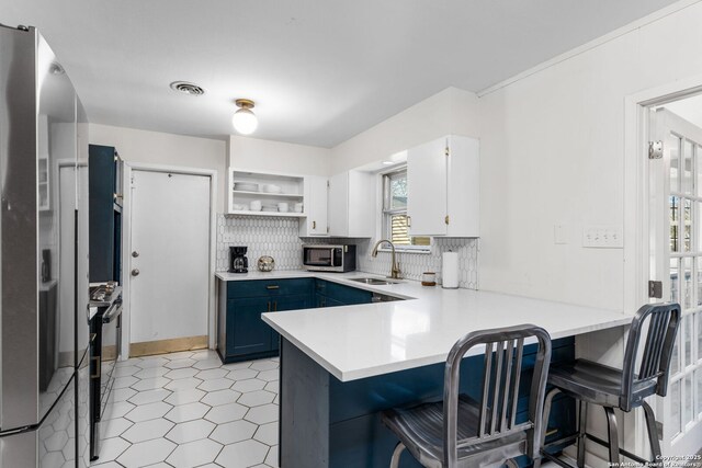 kitchen with a peninsula, stainless steel appliances, light countertops, open shelves, and a sink