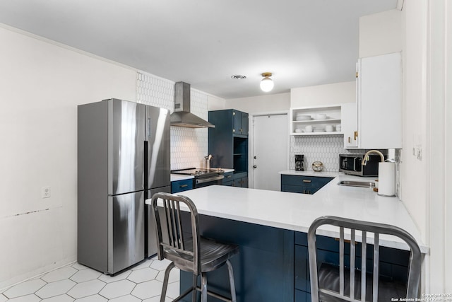 kitchen with blue cabinets, open shelves, a sink, appliances with stainless steel finishes, and wall chimney exhaust hood