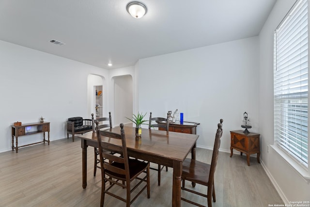 dining space featuring arched walkways, baseboards, a wealth of natural light, and light wood-style floors