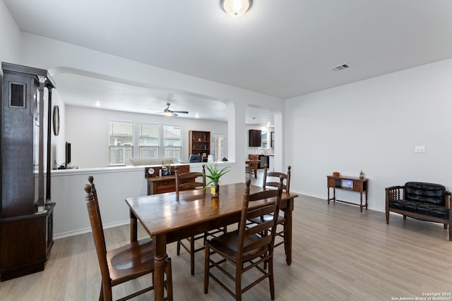 dining space with light wood-style floors, baseboards, visible vents, and arched walkways