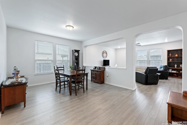 dining area with light wood-style flooring, arched walkways, and baseboards