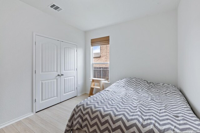 bedroom with a closet, wood finished floors, visible vents, and baseboards