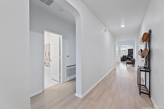 hall featuring light wood finished floors, visible vents, arched walkways, and baseboards