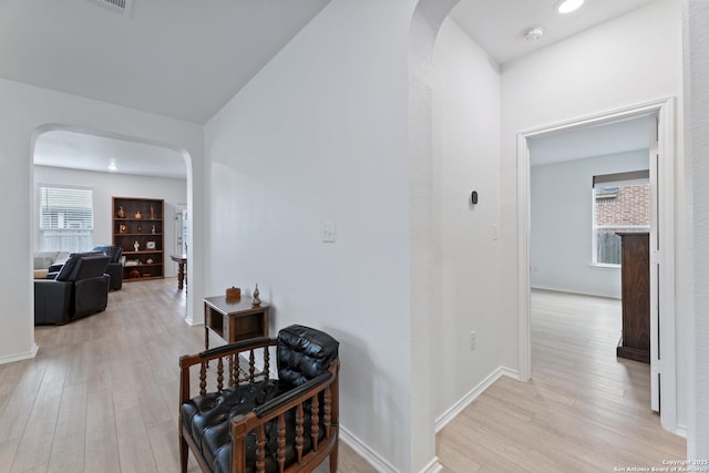 hall featuring light wood-type flooring, arched walkways, and baseboards