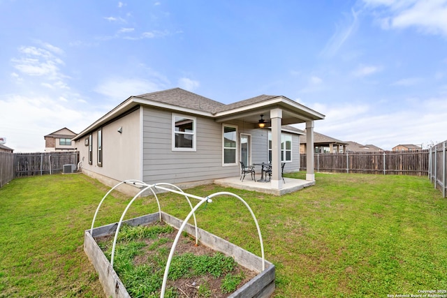 rear view of property featuring ceiling fan, a vegetable garden, a lawn, and a patio