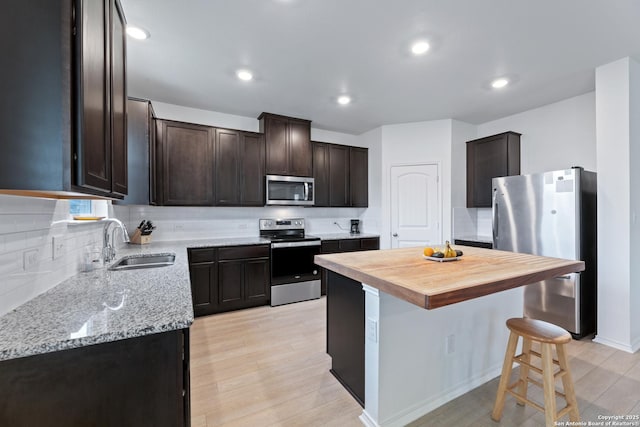 kitchen with dark brown cabinetry, decorative backsplash, light stone countertops, stainless steel appliances, and a sink