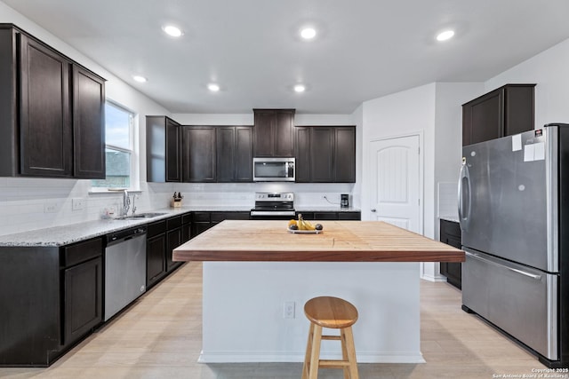 kitchen with a sink, dark brown cabinets, appliances with stainless steel finishes, backsplash, and a center island