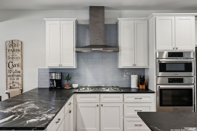 kitchen featuring appliances with stainless steel finishes, decorative backsplash, wall chimney exhaust hood, and white cabinets