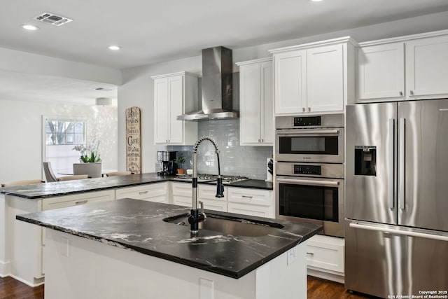 kitchen with a peninsula, visible vents, wall chimney exhaust hood, stainless steel appliances, and a sink