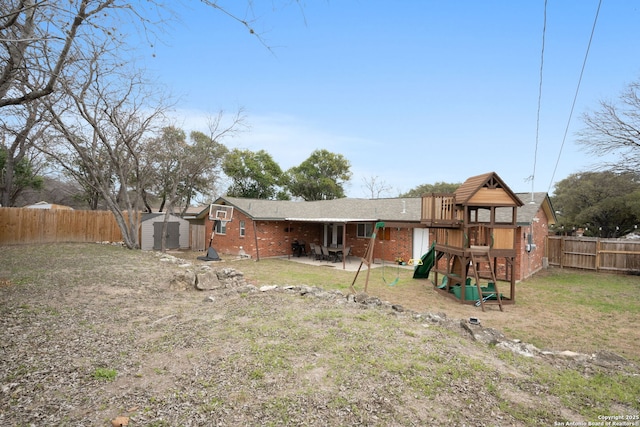 back of house with a playground, a fenced backyard, brick siding, an outdoor structure, and a storage unit