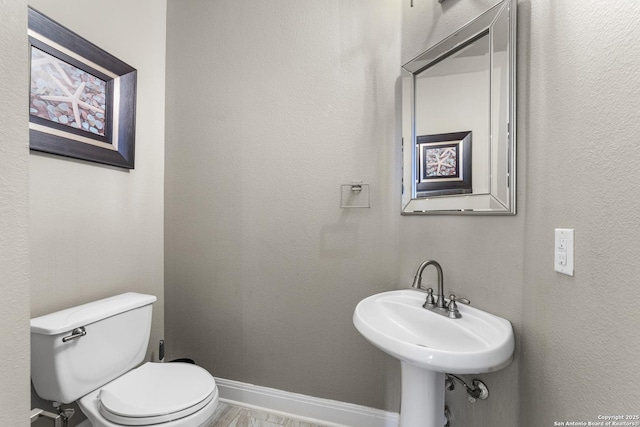 bathroom featuring toilet, baseboards, and a textured wall