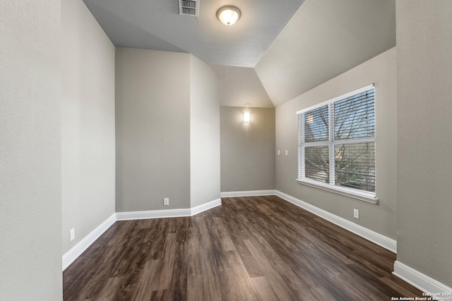 unfurnished room with vaulted ceiling, dark wood-style flooring, visible vents, and baseboards