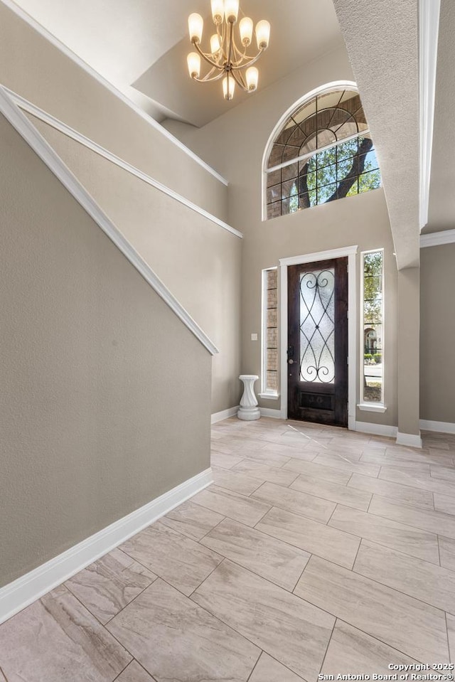 foyer entrance with a towering ceiling, baseboards, and a notable chandelier