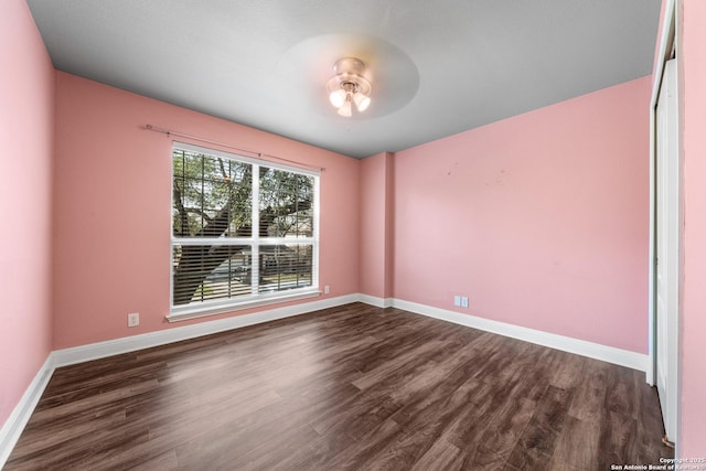 spare room with baseboards and dark wood-style flooring