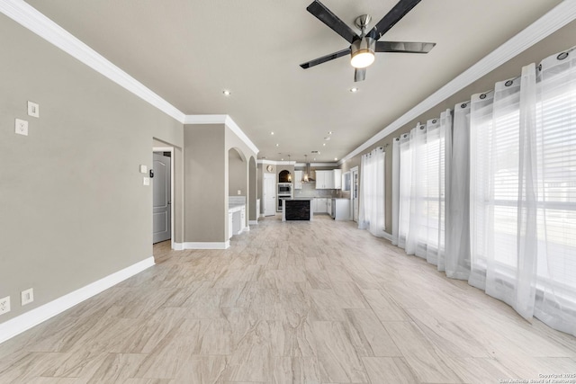 unfurnished living room with arched walkways, crown molding, recessed lighting, a ceiling fan, and baseboards