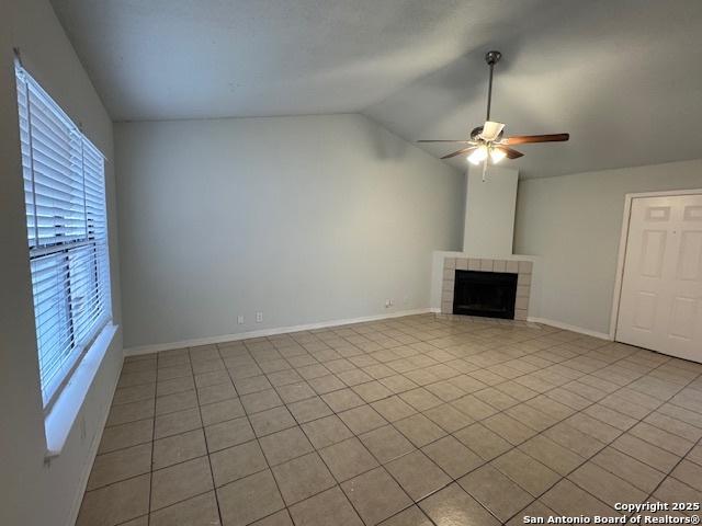 unfurnished living room with lofted ceiling, tile patterned flooring, a fireplace, a ceiling fan, and baseboards