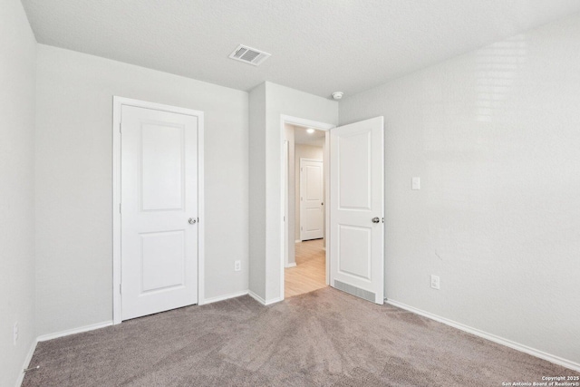 unfurnished bedroom with carpet, a textured ceiling, visible vents, and baseboards