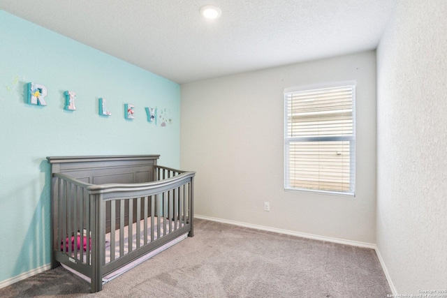 carpeted bedroom featuring a textured ceiling, a crib, and baseboards