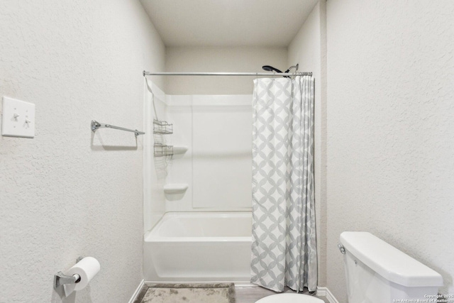 full bath featuring a textured wall, toilet, and shower / tub combo with curtain