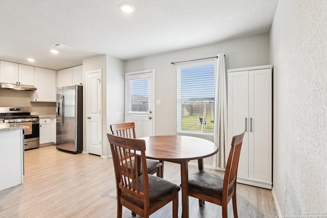 dining room featuring visible vents, a textured wall, light wood-style flooring, a textured ceiling, and baseboards